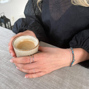 Stilrent armband med små pärlor i blå spetsagat med mönster i blått, turkos, grått och jordnära nyanser samt detaljer i platinapläterad 925 sterling silver från Livingstone Wikh Accessories.